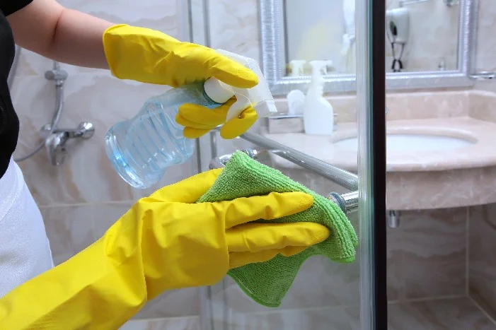 Person reinigt Duschtür mit Lappen